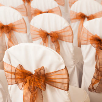 White wedding bouquet in the background with chairs in foreground arranged in rows and dressed with ribbons