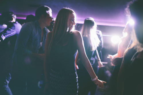 Blonde woman dancing alone amongst a group of people partying in a night club