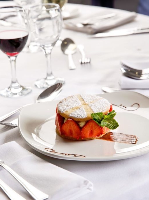 Strawberry dessert on white plate on a white table with a glass of red wine