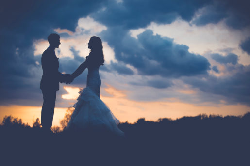 Bride and groom hold hands with dusk sky in background